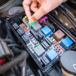 Hand checking a fuse in the fuse box of a modern car engine