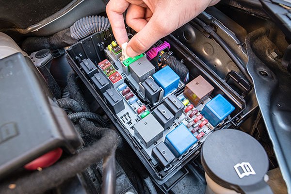 Hand checking a fuse in the fuse box of a modern car engine